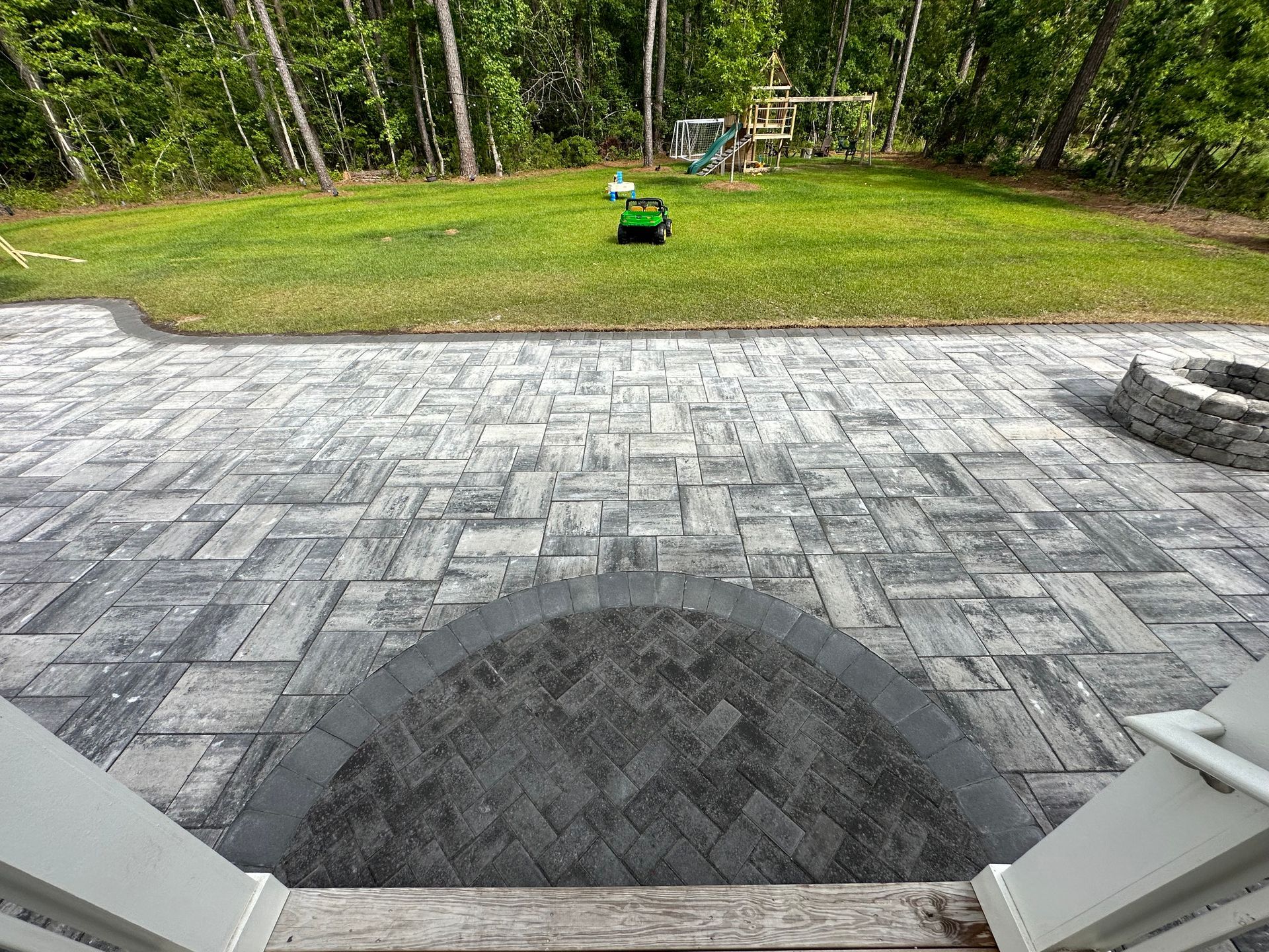 Stone patio leading to grassy yard with robot mower and trees.