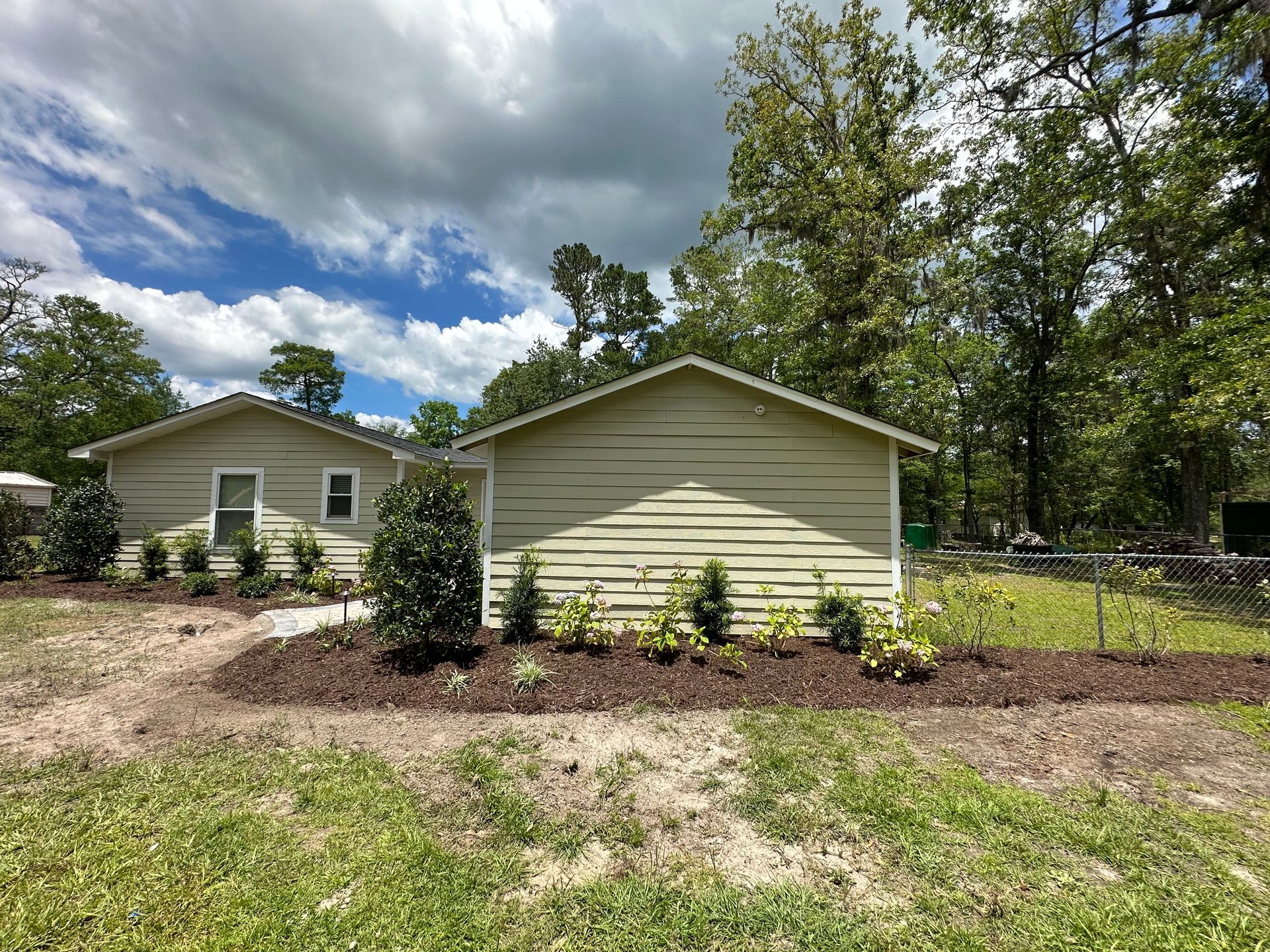 Two light green houses with dark brown mulch and green plants. Blue sky with white clouds.
