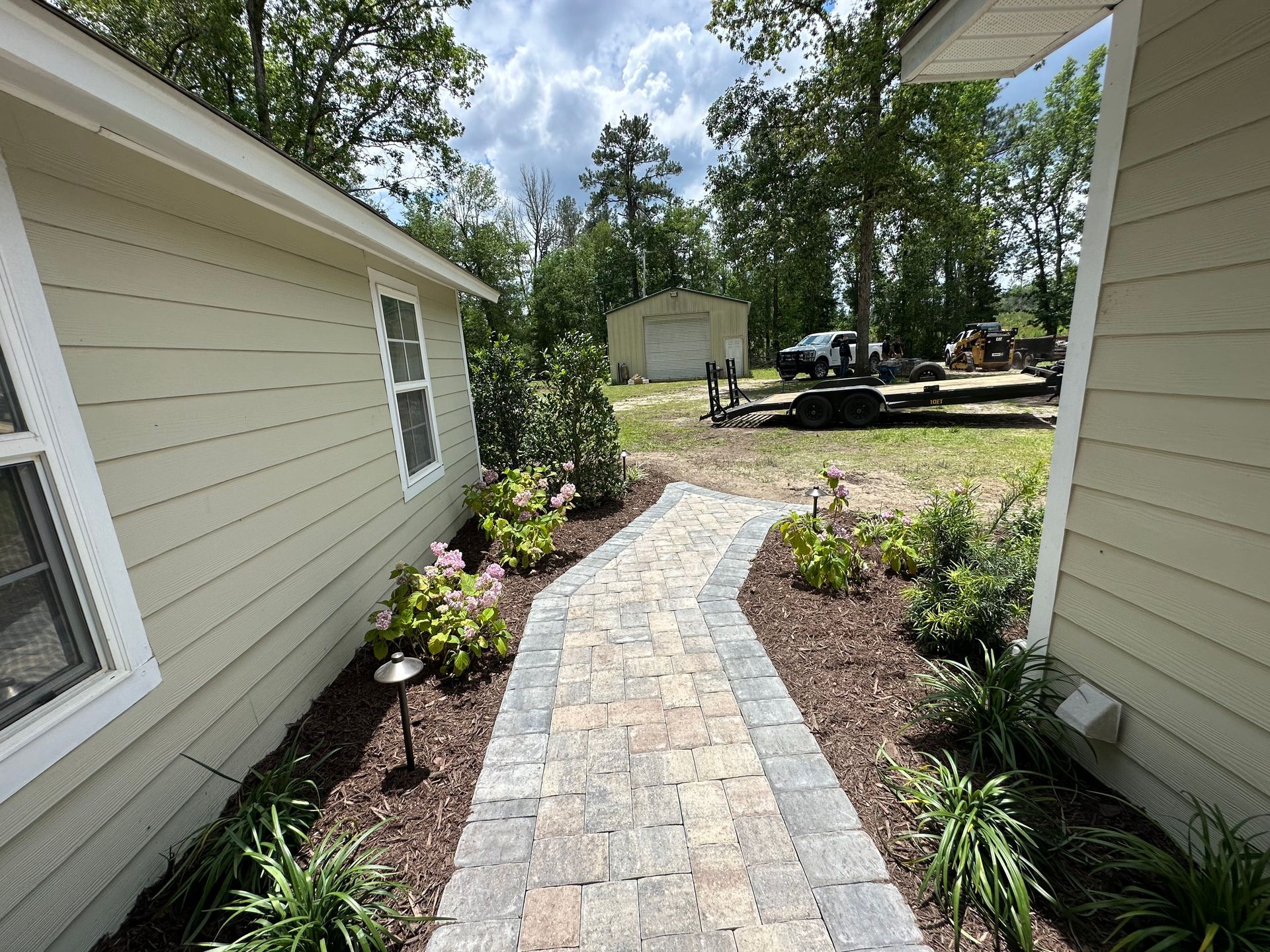 Stone walkway flanked by flower beds, leading to a shed in a backyard setting.