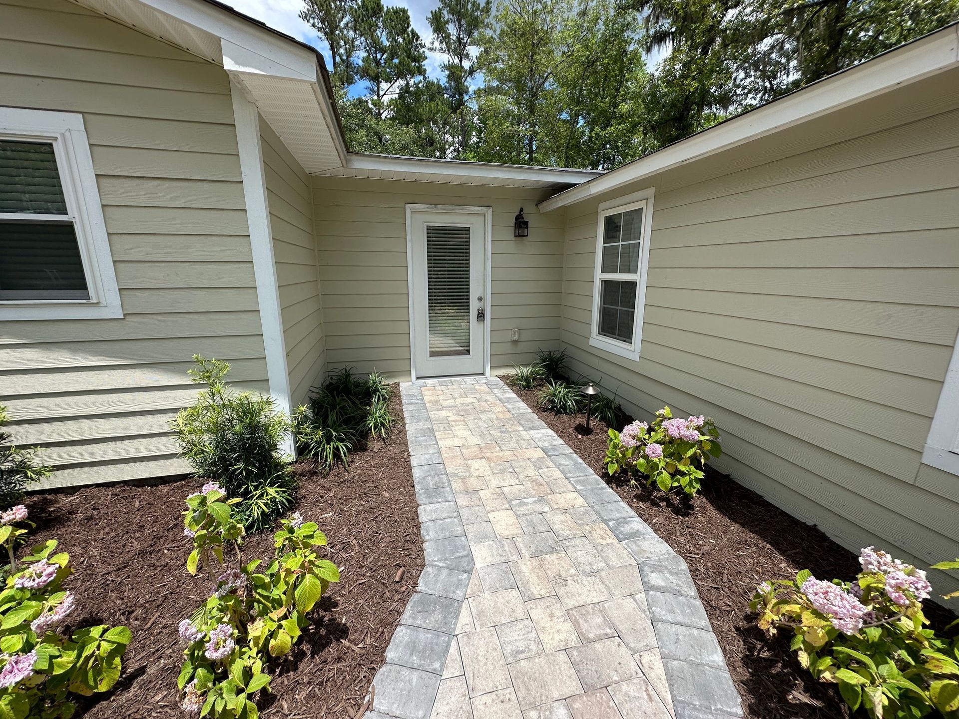 Paver walkway leads to a front door with sidelights, flanked by flower beds and tan siding.