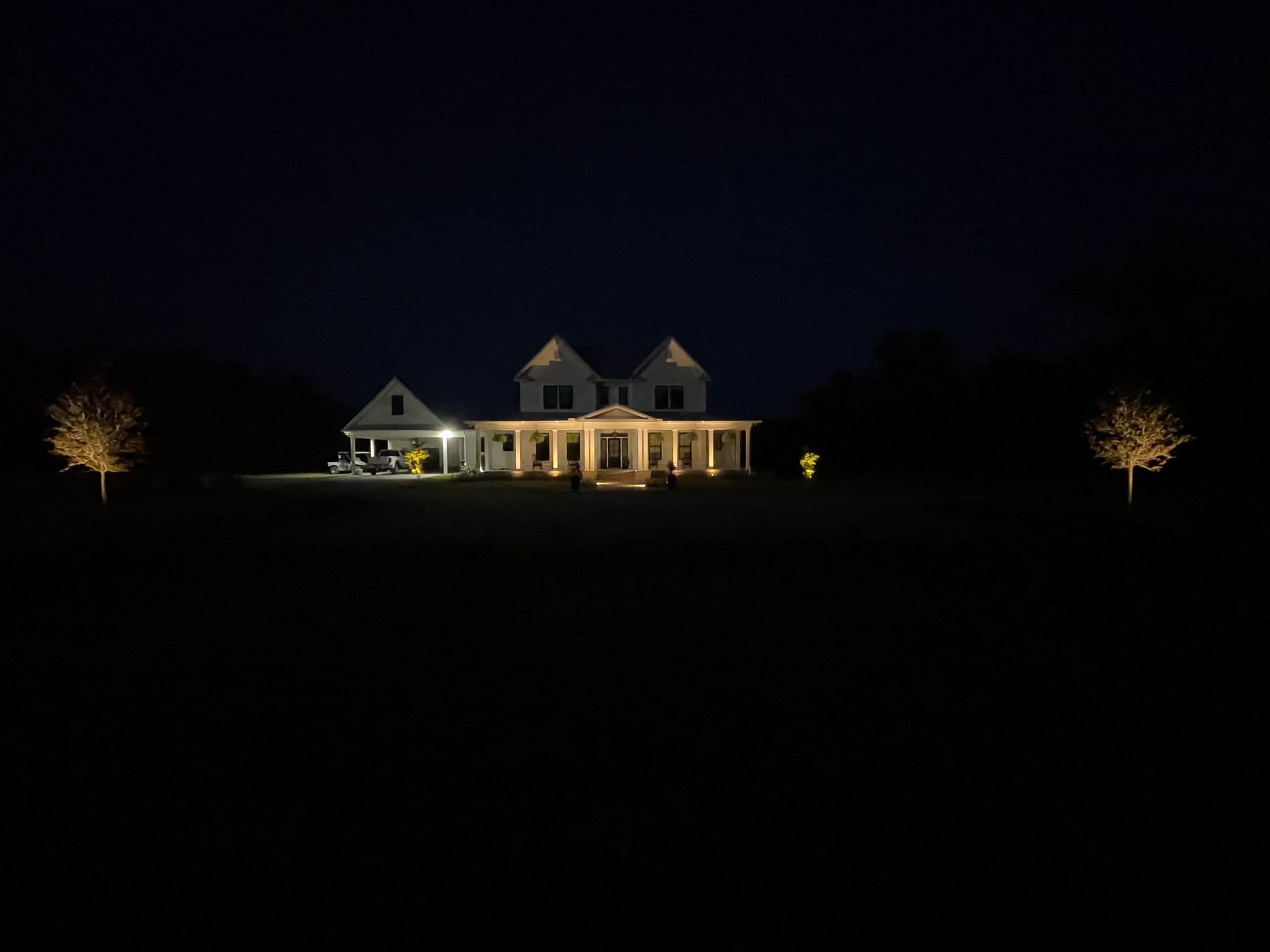 Illuminated white house at night with trees on either side, set against a dark sky.