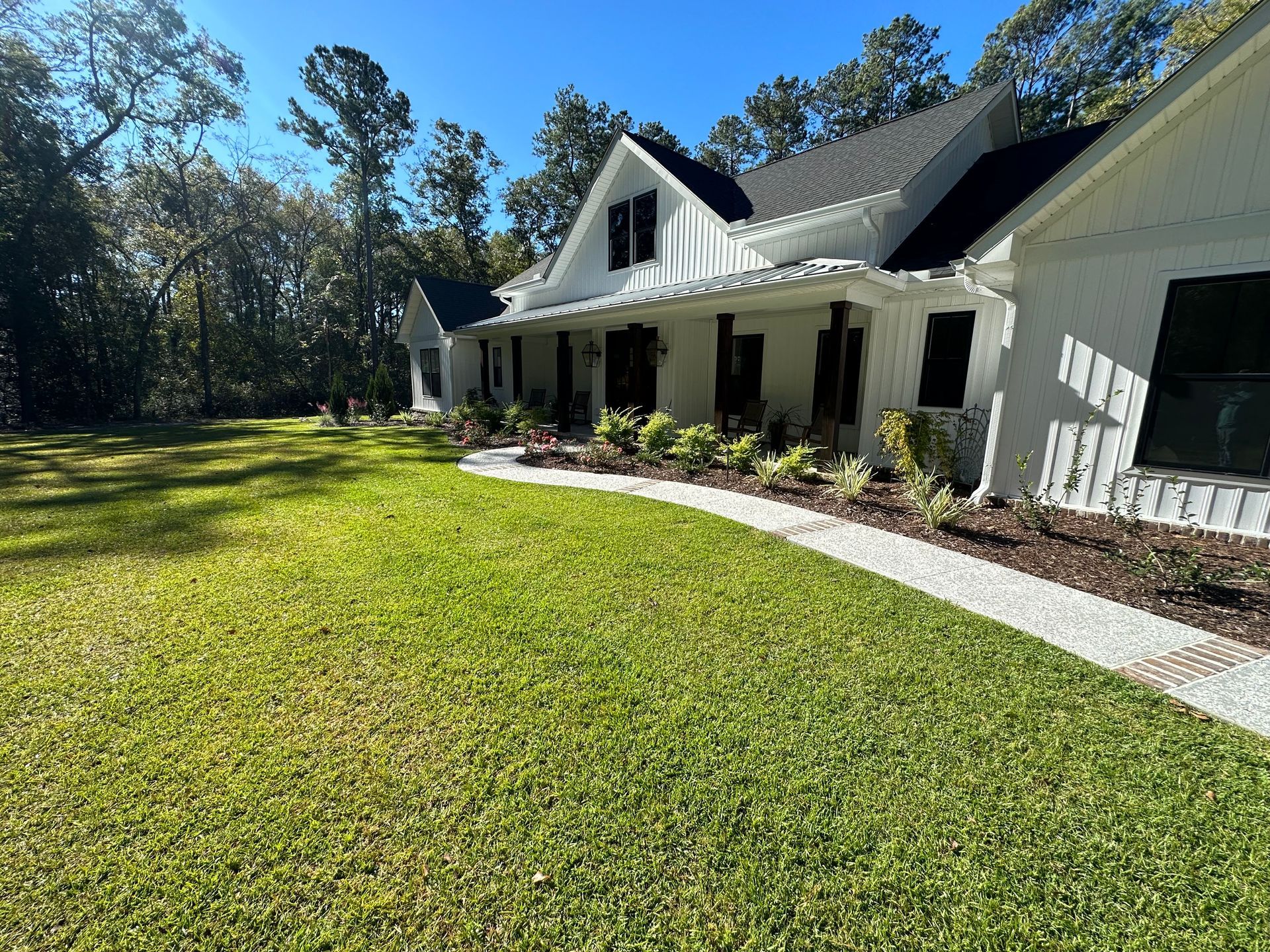 White house with black shutters, on a green lawn with a stone walkway, under a blue sky.