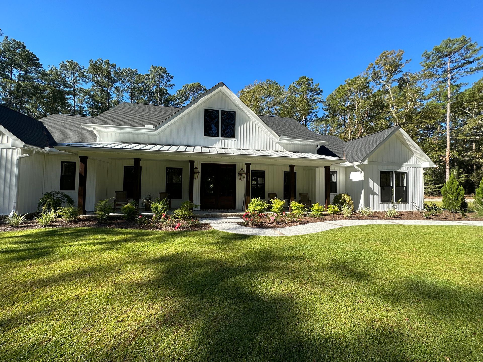 White farmhouse with black trim, green lawn, blue sky, trees in background.
