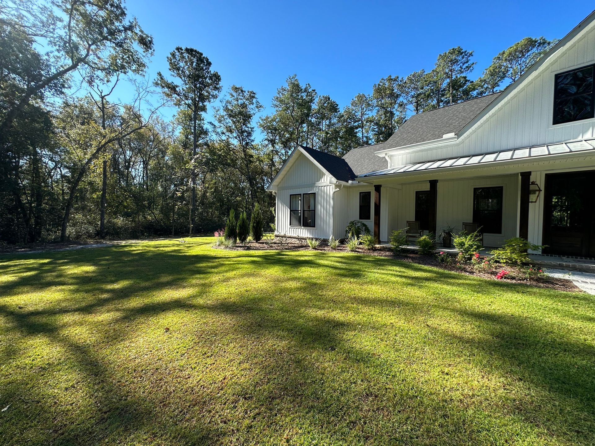 White farmhouse with green lawn and trees under a clear blue sky.