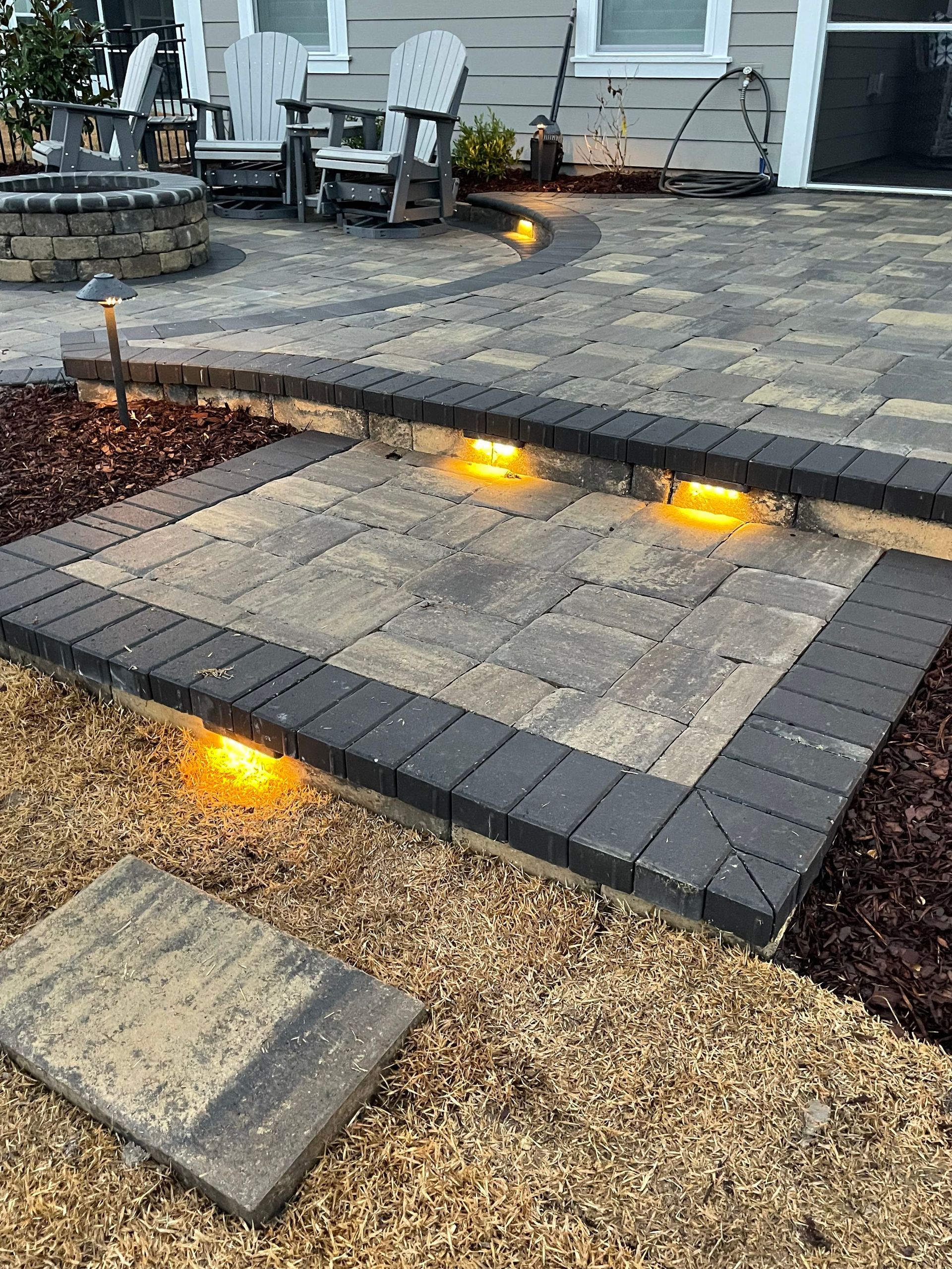 Paver patio with steps and built-in lighting.  Dark edging contrasts light grey pavers.