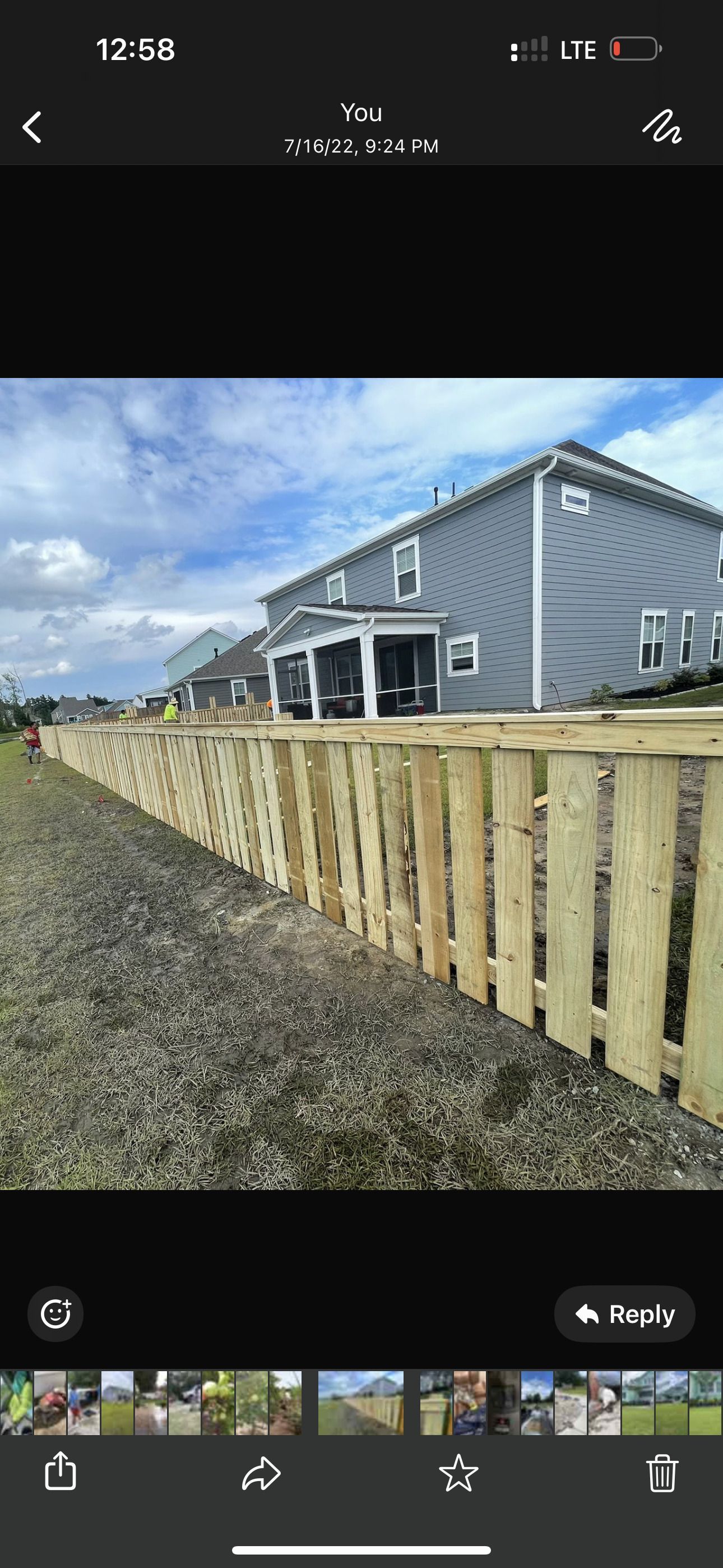 A wooden fence lines a gravel driveway next to a blue house on a sunny day.