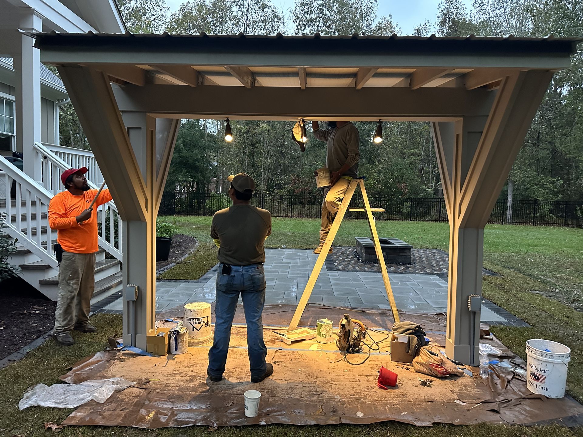 Men installing lights on a wooden structure outdoors. One on a ladder, two others watch.