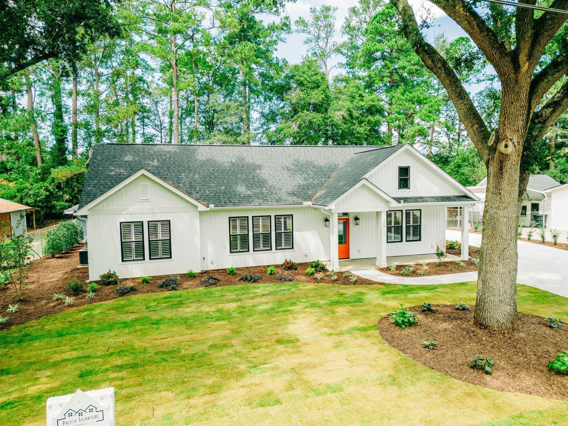 White farmhouse with black trim, orange door, and a tree in front.
