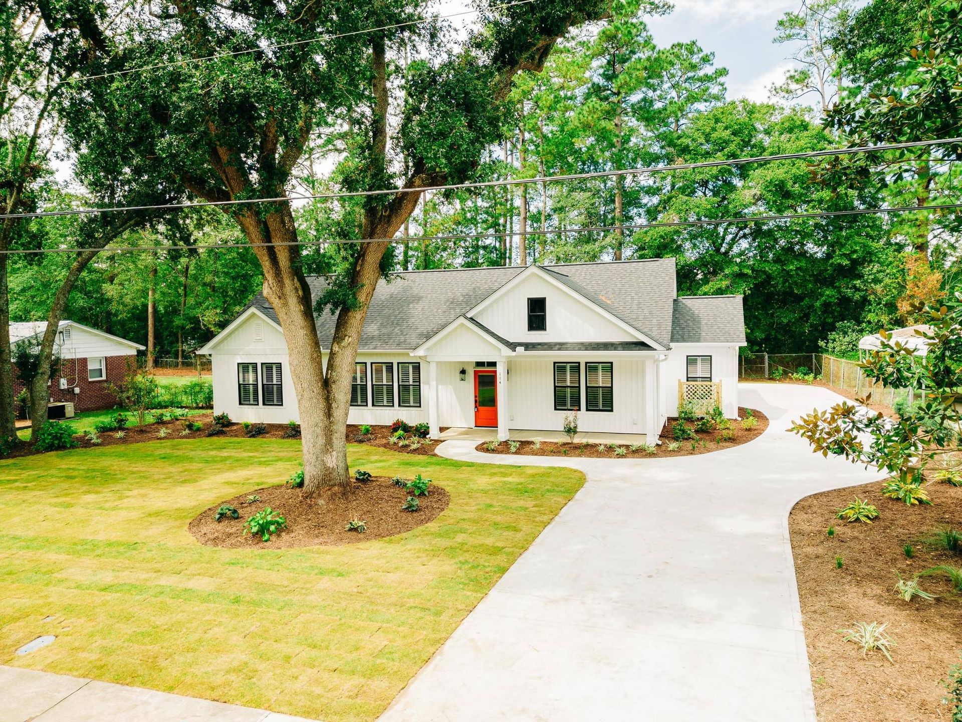 White house with red door, concrete driveway, and large tree in front yard.
