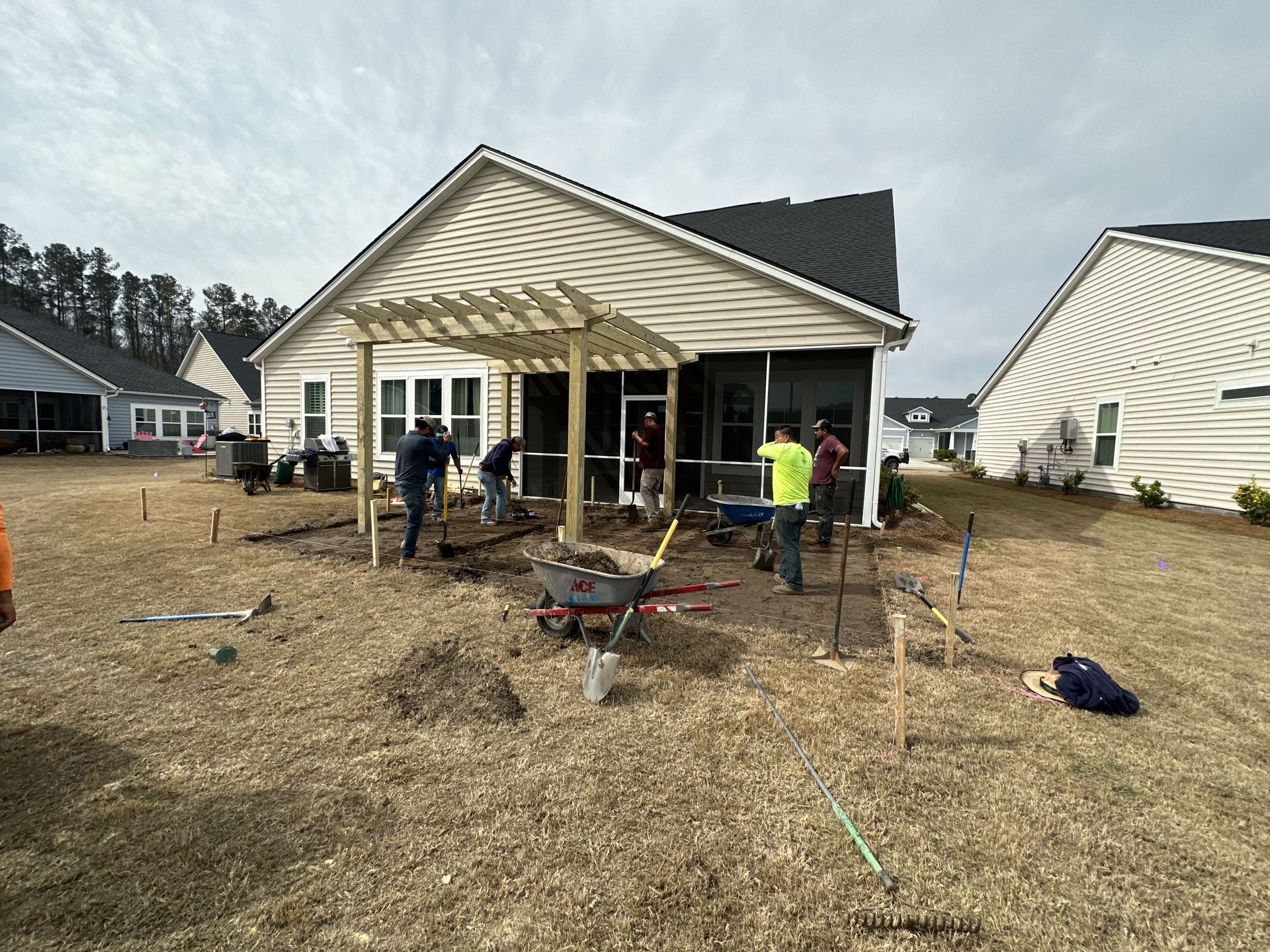 Construction crew working on a patio with pergola in a backyard. Workers are installing pavers.