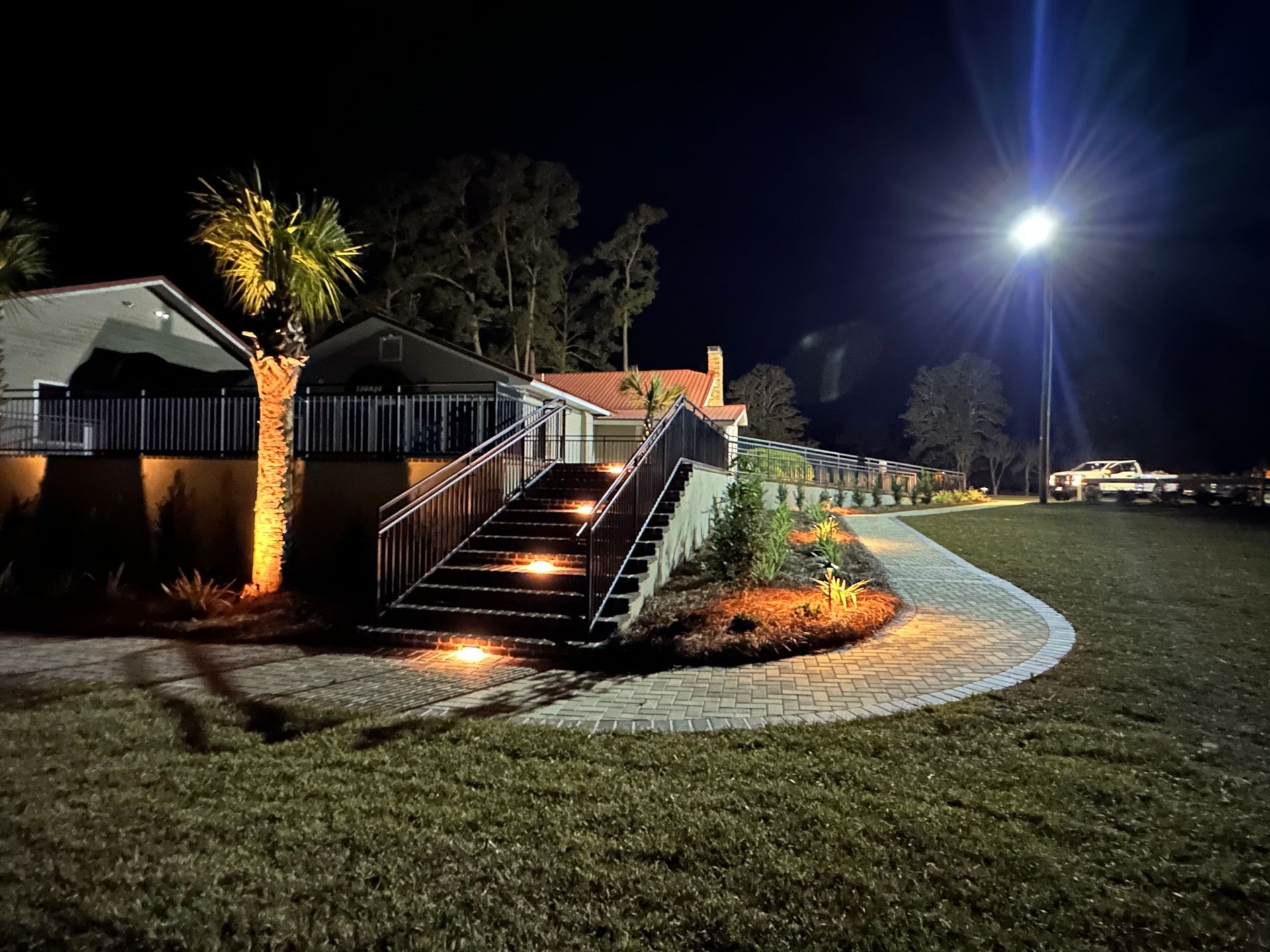 Night scene: lit stairs leading to a building with landscaping. Bright overhead light.