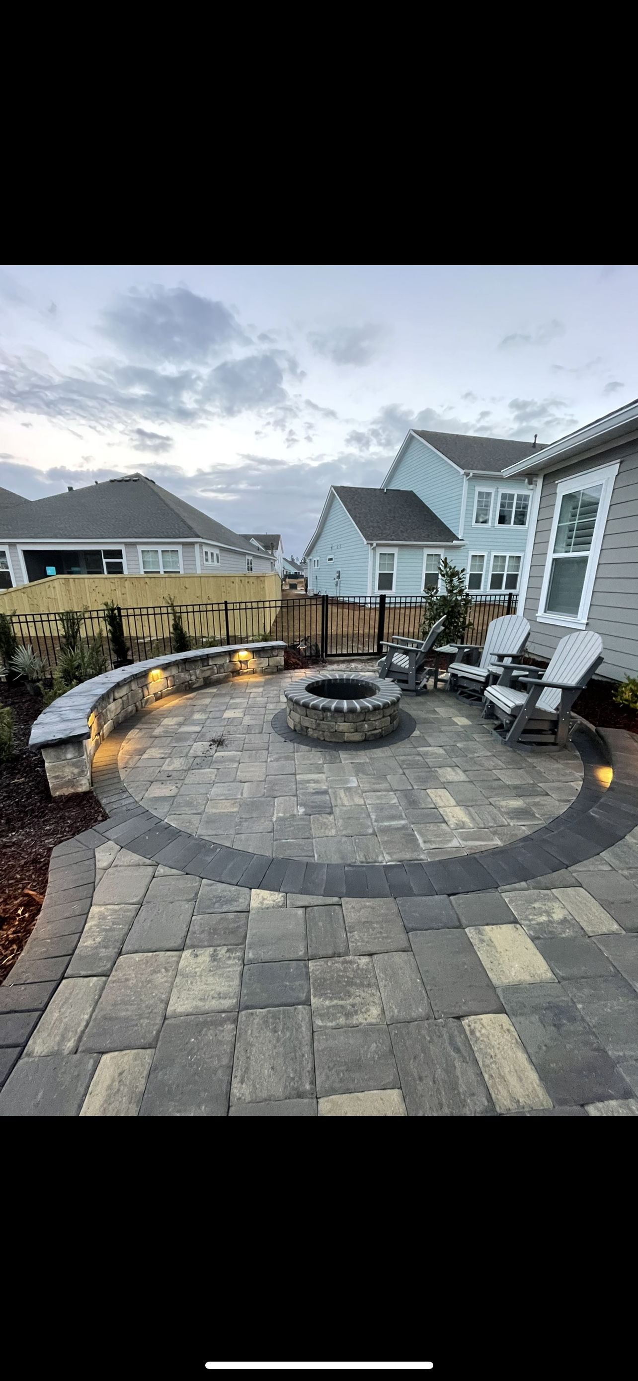 Stone patio with fire pit, seating, and surrounding houses under an overcast sky.