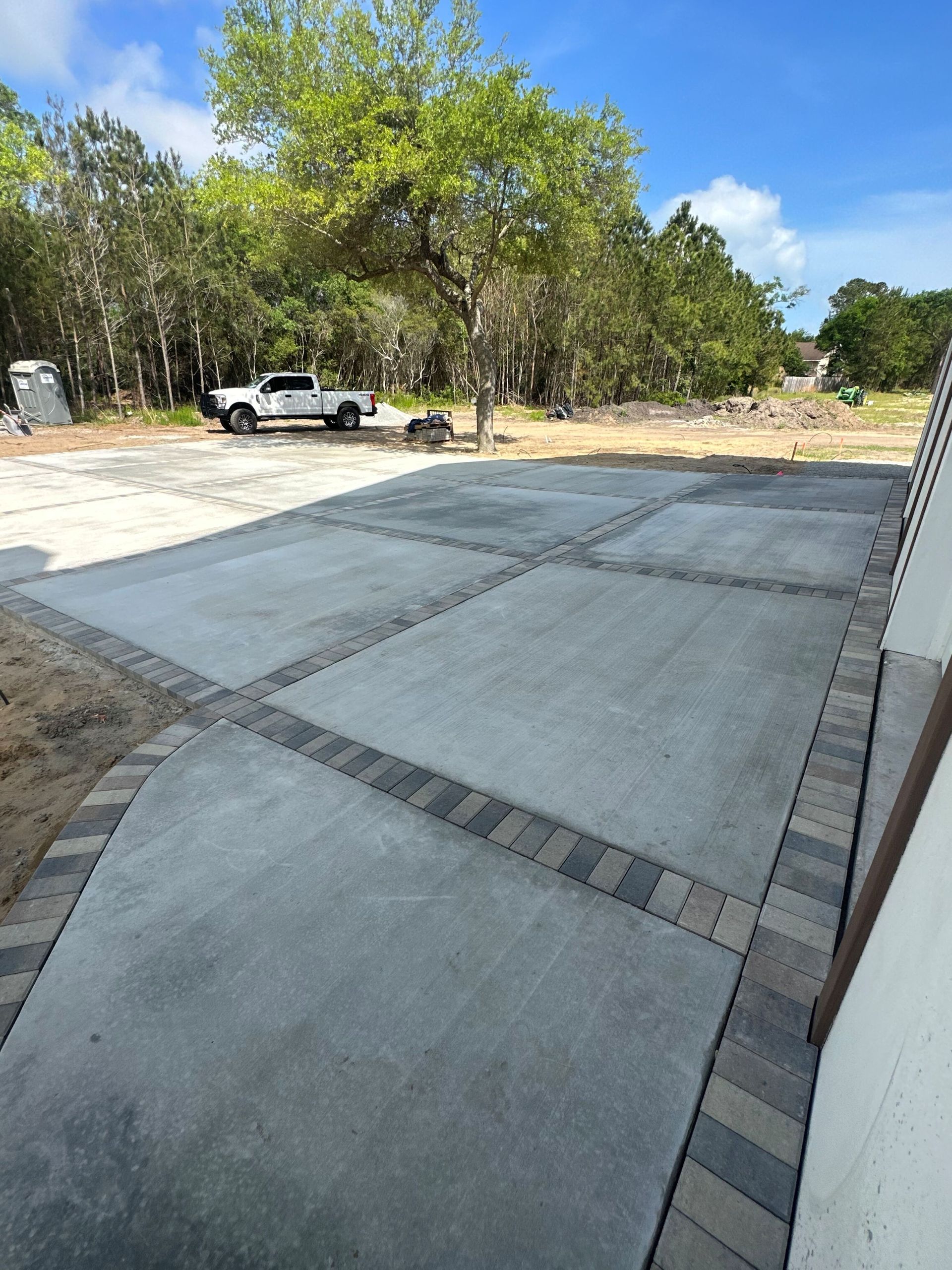 Concrete driveway with brick borders; a white truck is in the background, and trees surround the area.