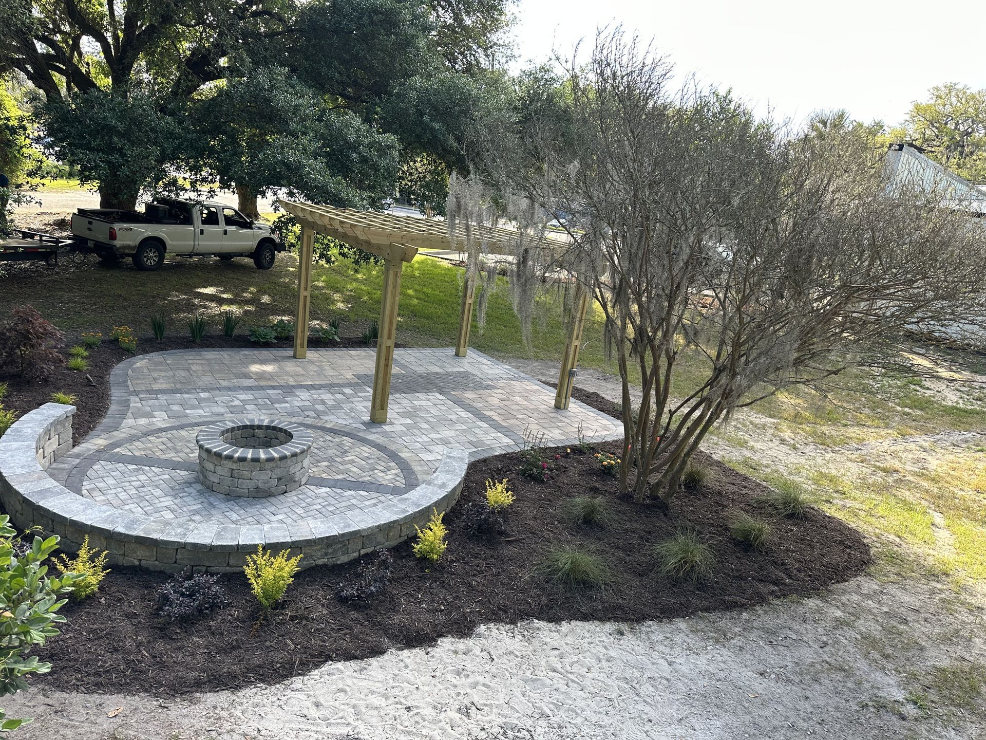 Stone patio with pergola and fire pit, surrounded by plants and landscaping.