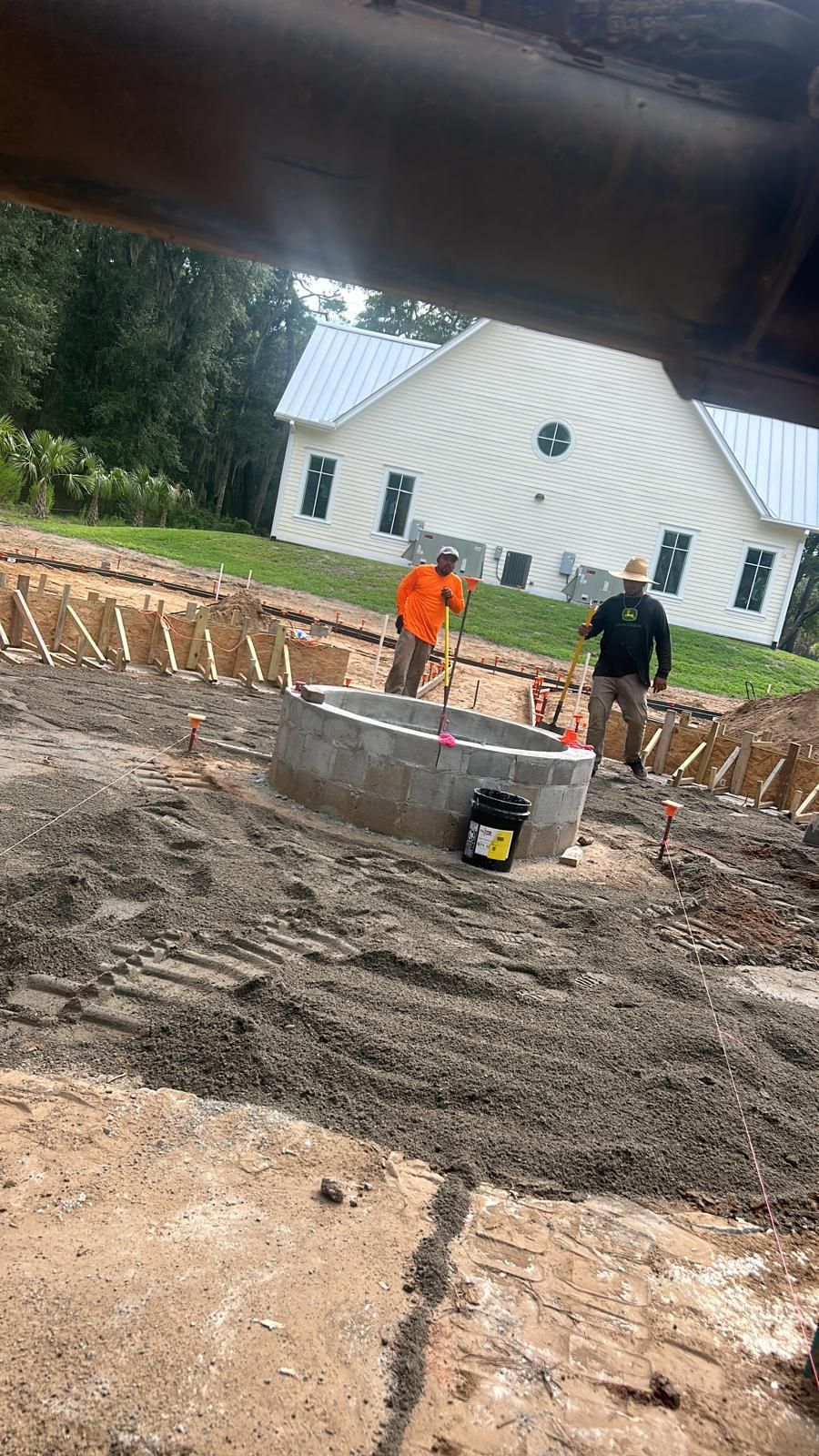 Construction site with workers, concrete ring, house in background.