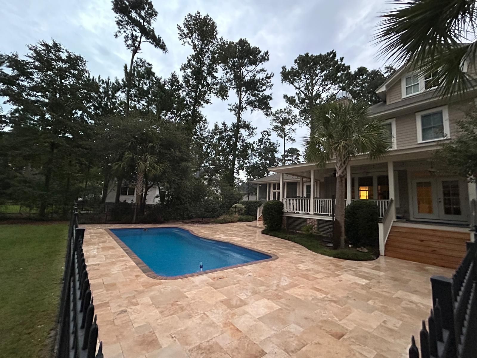 Backyard with a pool, patio, and two-story house under a cloudy sky.
