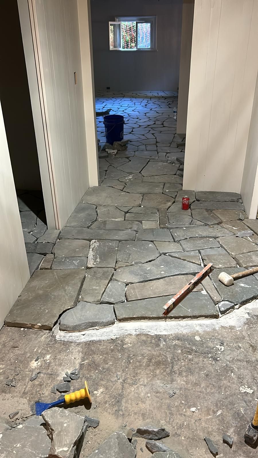 Interior hallway during stone tile installation, scattered tiles on floor, tools visible.