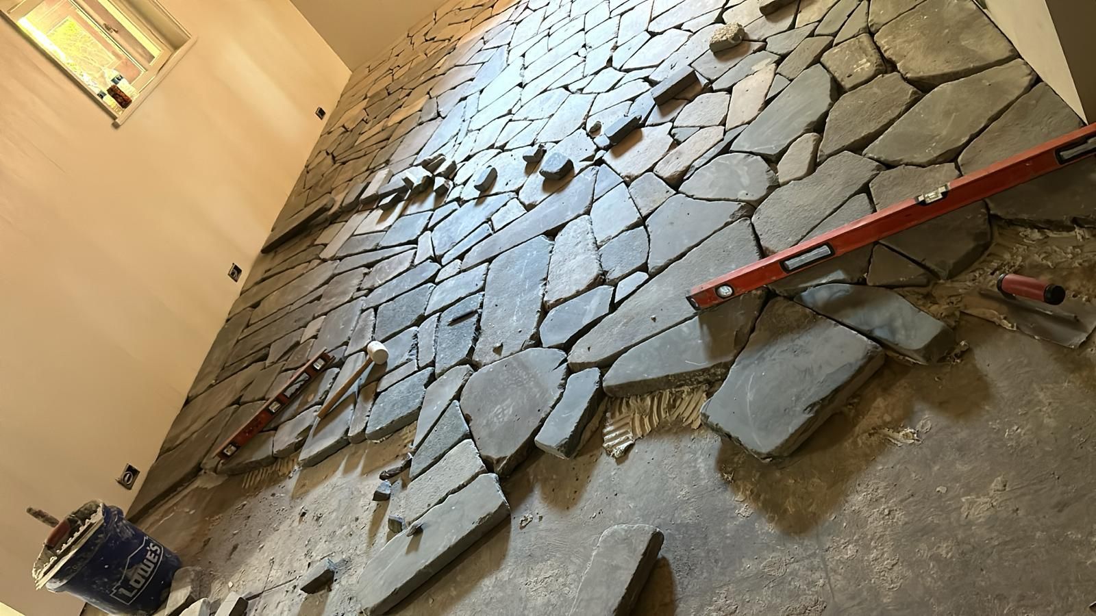 Installation of irregularly shaped gray stone tiles on a wall; construction in progress.