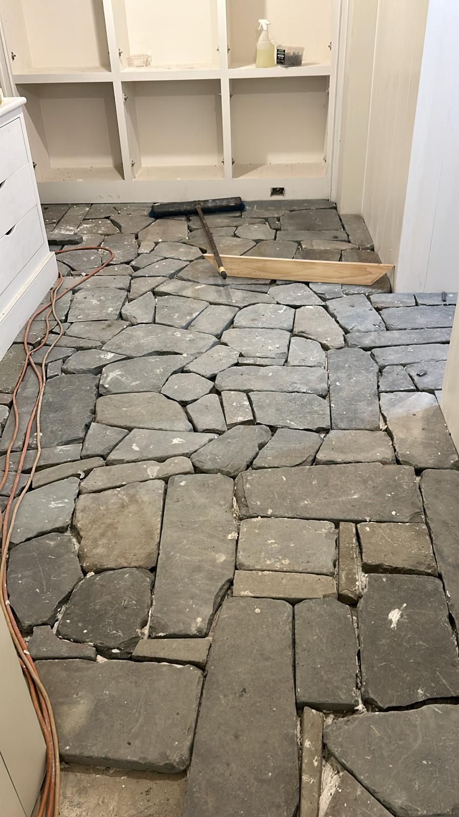 Stone floor being installed in a room with white shelves and walls.