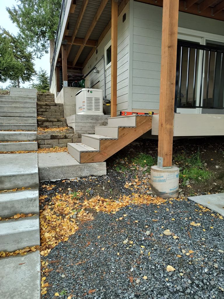 Unfinished outdoor staircase beside a house, with concrete steps, wood supports, and gravel below.
