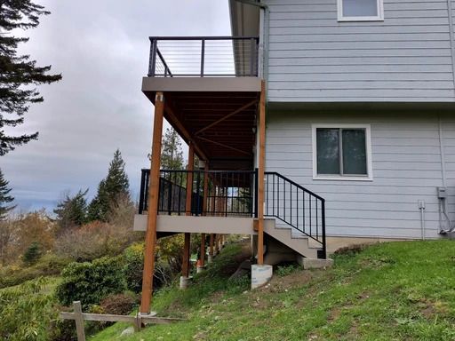Back porch deck with stairs attached to a light blue house on a grassy hillside