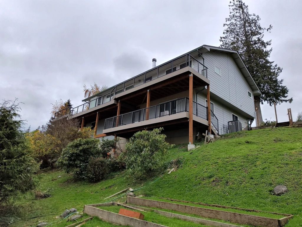 Two-story house with a covered porch on a grassy hillside under a cloudy sky