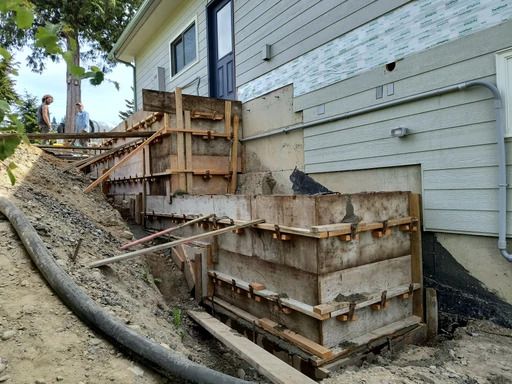 Wooden retaining walls under construction beside a house on a sloped yard