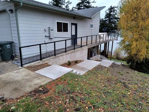 Side-access ramp with black railings leading to a raised white house beside a sloped yard.