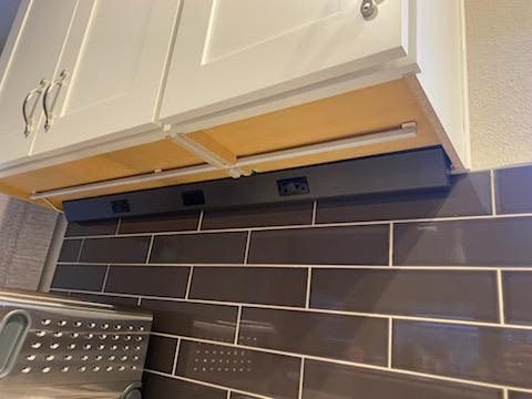 Kitchen cabinets above a dark tile backsplash with a stainless dish rack on the counter