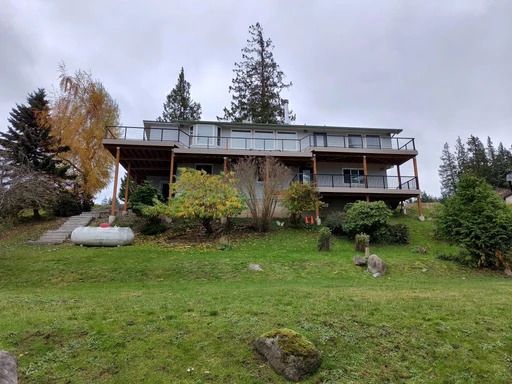 House on a grassy hillside with a deck, trees, and overcast sky
