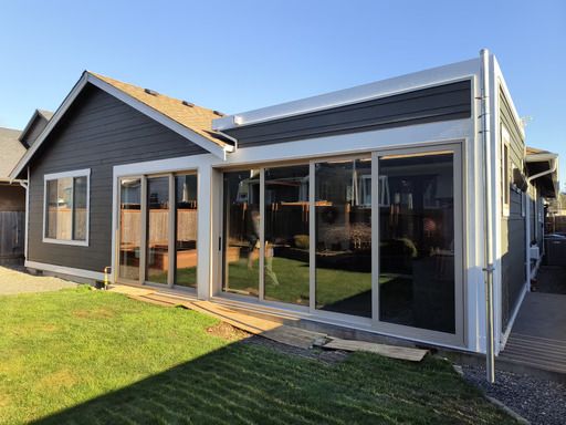 Modern gray house with large glass sliding doors and a covered patio, viewed from a grassy backyard
