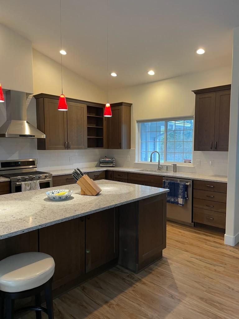 Modern kitchen with dark cabinets, granite island, red pendant lights, and a window over the sink.