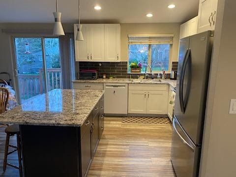 Modern kitchen with granite island, white cabinets, stainless fridge, and wood-look flooring