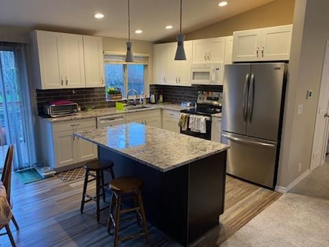 Modern kitchen with island, stainless fridge, pendant lights, and stools by a window