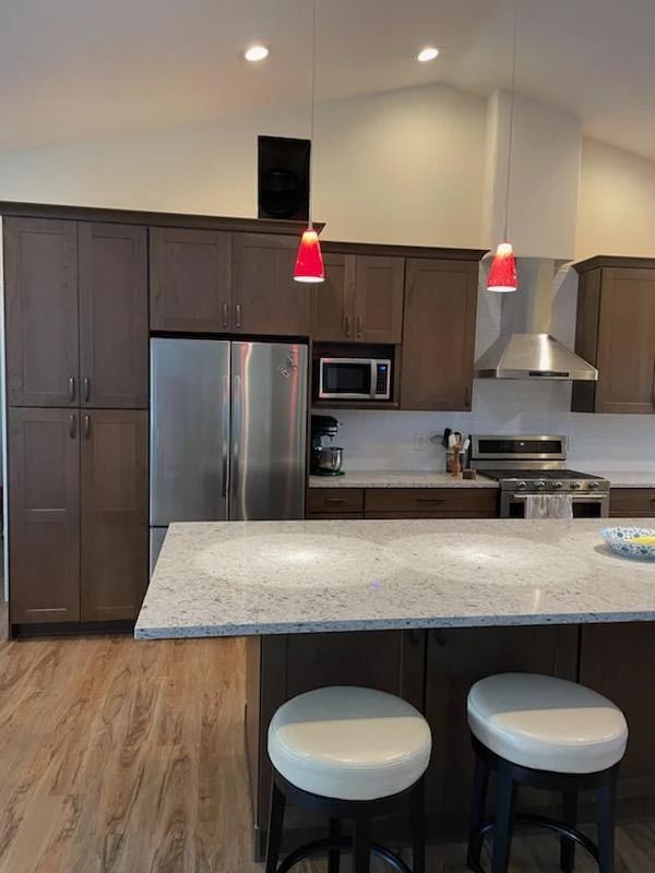 Modern kitchen with stainless appliances, gray cabinets, granite island, and two stools under red pendant lights