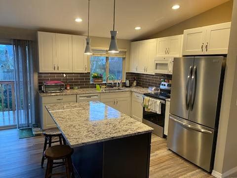 Modern kitchen with granite island, stainless steel appliances, white cabinets, and pendant lights