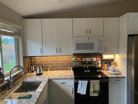 Bright kitchen with white cabinets, black stove, brick backsplash, and a window over the sink