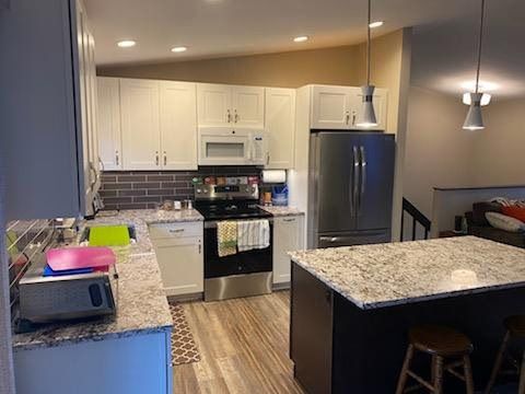 Modern kitchen with white cabinets, stainless appliances, granite island, and wood flooring