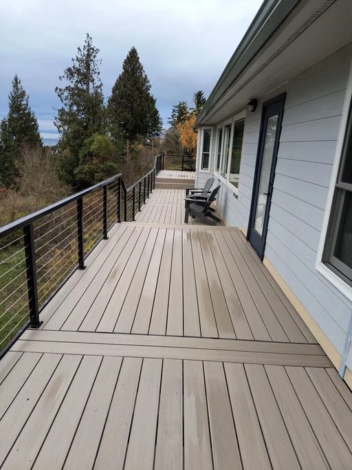 Modern deck with gray flooring, black railing, and a chair beside a house, overlooking trees and hills