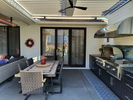 Covered patio with dining table, grill, black cabinets, and sliding glass doors