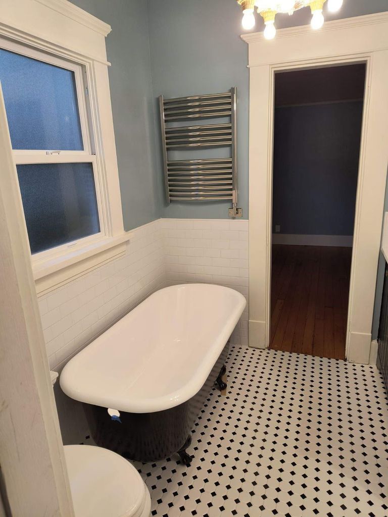 Small bathroom with white clawfoot tub, black-and-white tile floor, window, and towel rack.