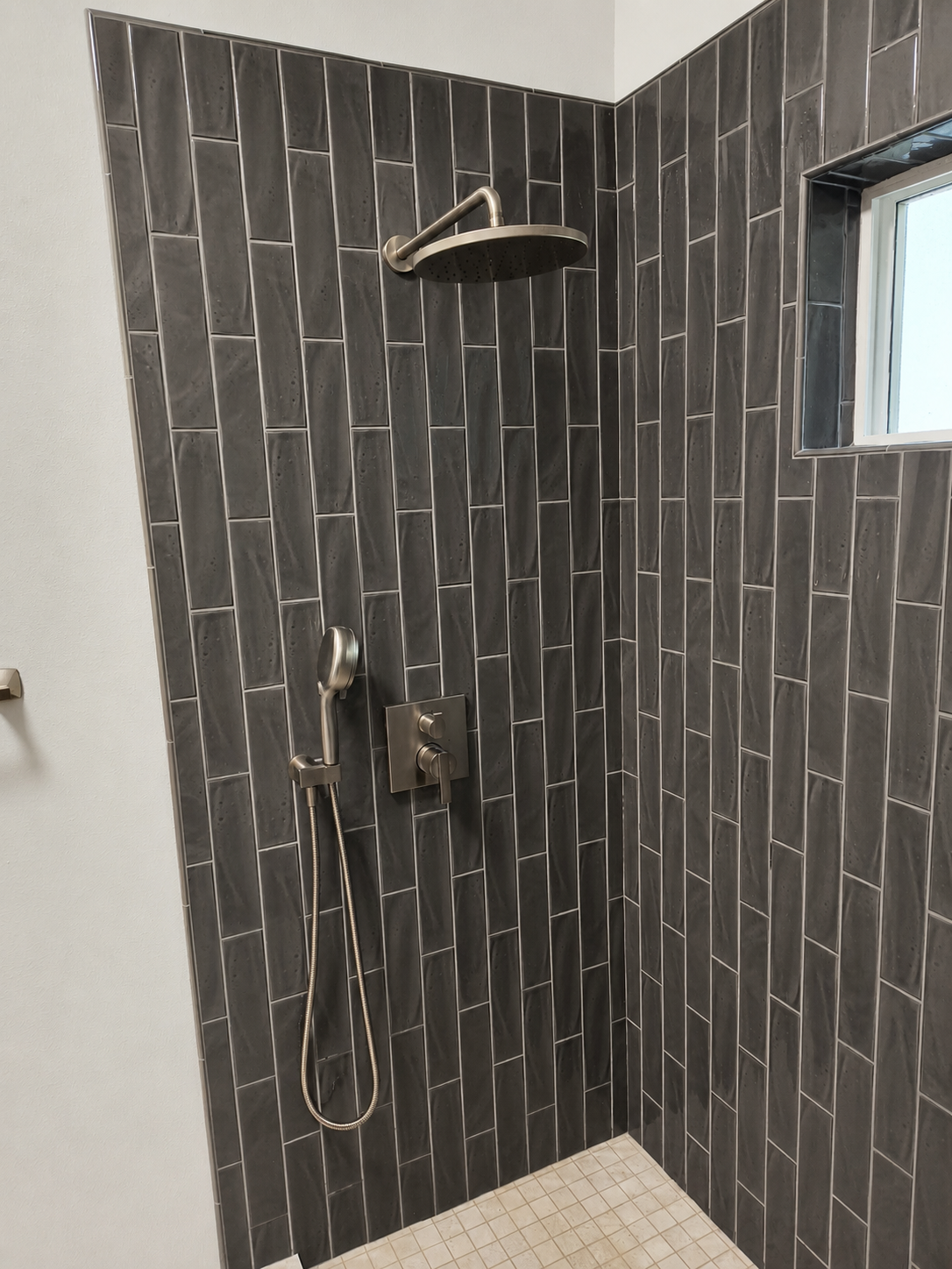 Custom dark tile walk-in shower with a rainfall showerhead in a bathroom remodel in Bellingham, WA by Alderwood Builders LLC.