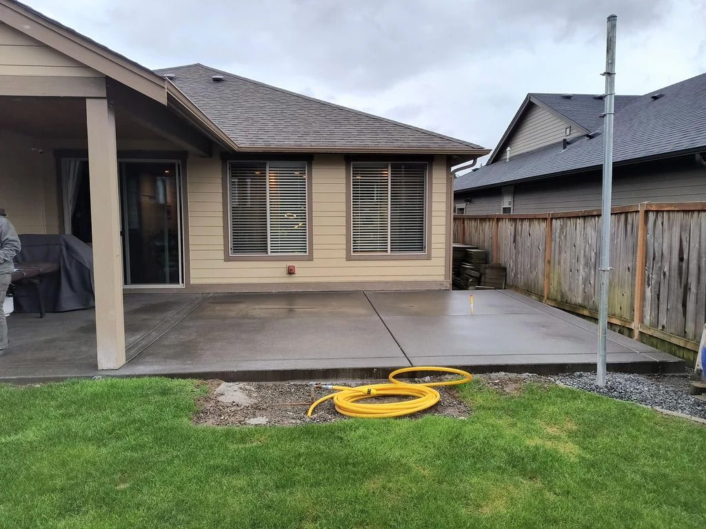 Backyard patio with a covered concrete slab, grass, fence, and a yellow garden hose in the foreground