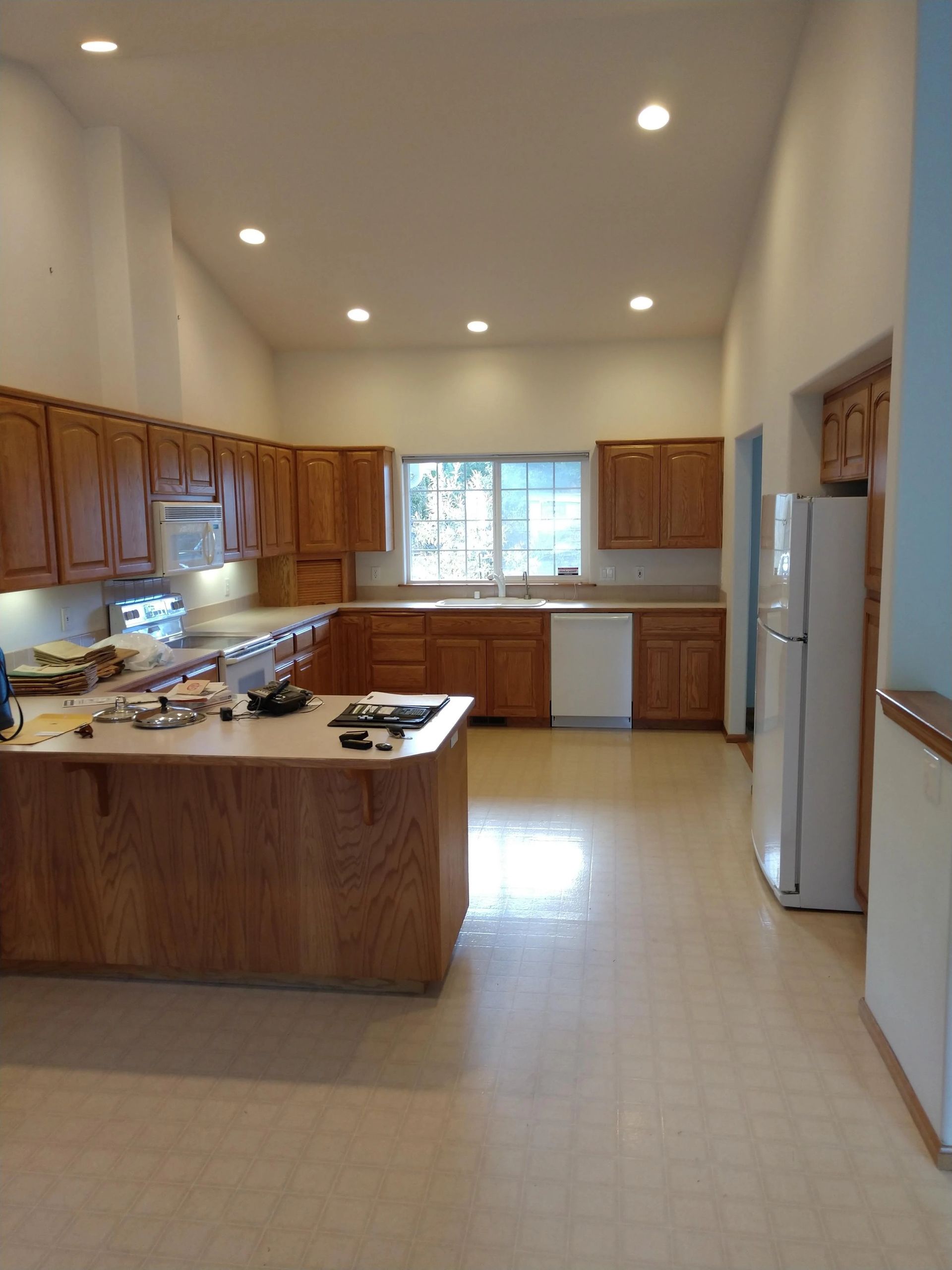 Spacious kitchen with wooden cabinets, white appliances, tiled floor, and a central island.