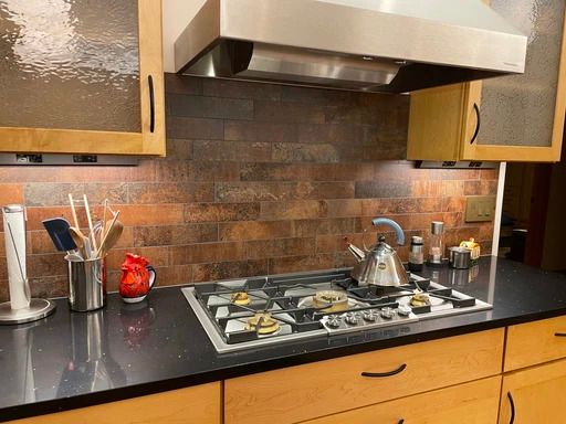 Modern kitchen stove with pots, red teapot, and black countertop beneath a stainless steel range hood