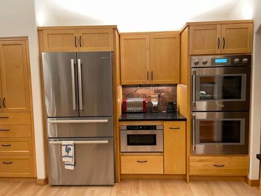 Modern kitchen with stainless steel refrigerator, built-in ovens, and light wood cabinets