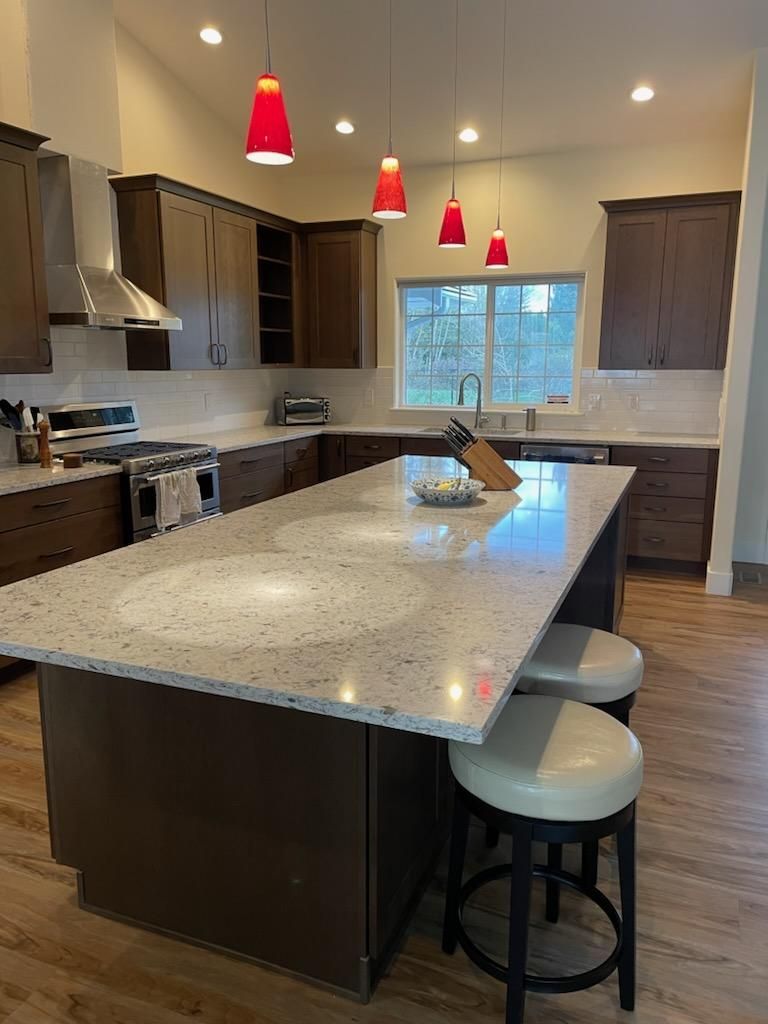 Modern kitchen with large island, pendant lights, dark cabinets, and stools by the counter