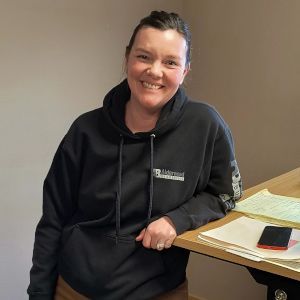 Alisa Bouwman in a black hoodie seated at a desk with papers and a phone