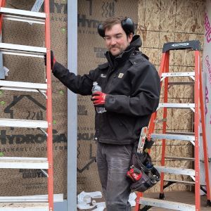 Construction worker in hard hat and harness standing outdoors beside a metal building frame