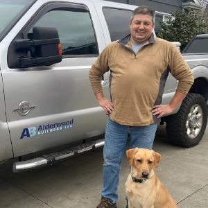 Man standing beside a silver truck with an Aidenwood Builders logo, with a tan dog in front of him.